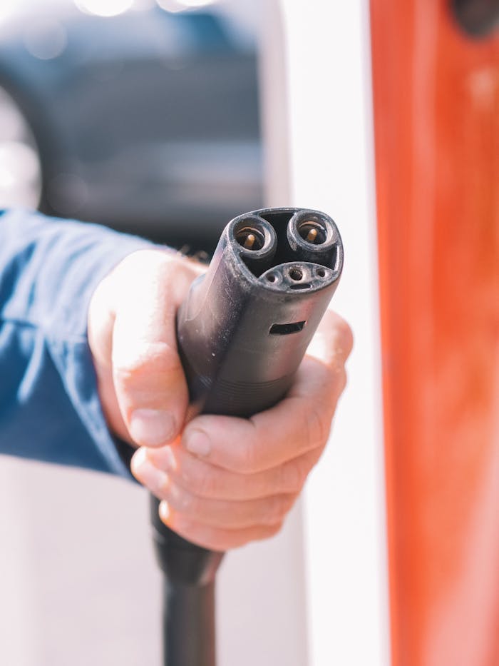 who-we-are Close-up of a person holding an electric car charging plug, representing renewable energy use.